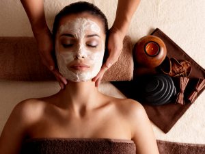 Spa massage for young woman with facial mask on face - indoors